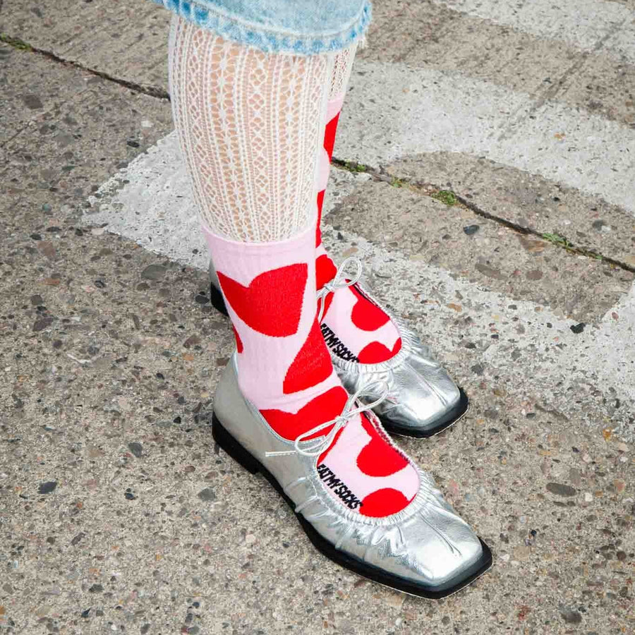 Chaussettes roses à grands cœurs rouges portées avec des ballerines argentées