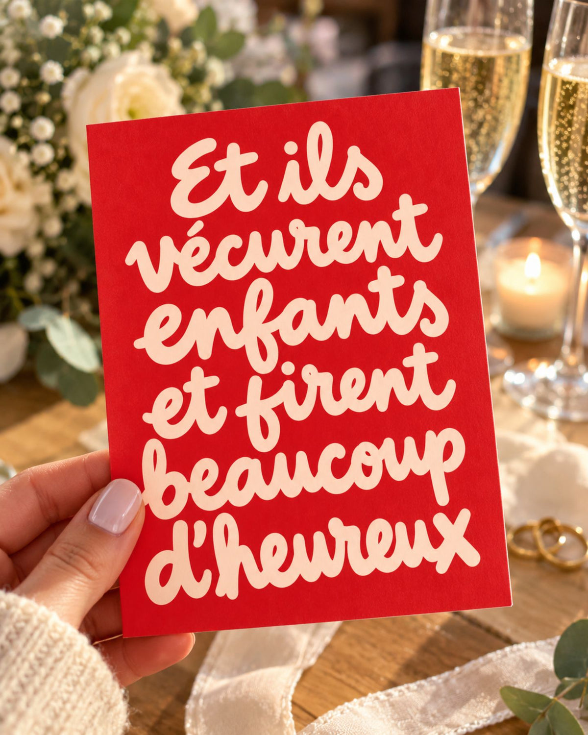 Carte rouge au lettrage manuscrit crème, tenue près de flûtes de champagne