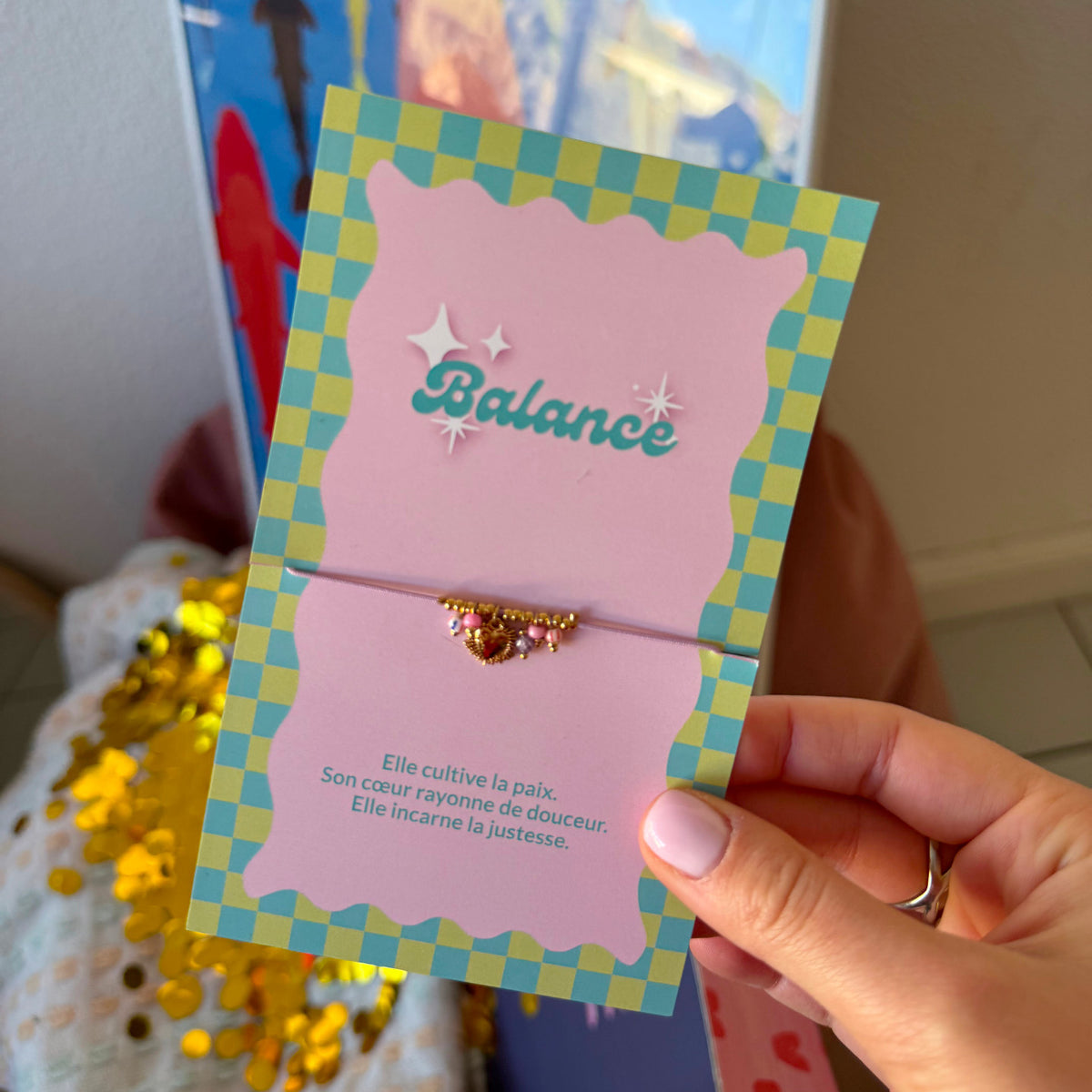 Bracelet Balance doré à perles roses, présenté sur une carte à damier turquoise