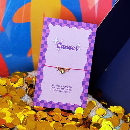 Bracelet Cancer à cordon rose, perles dorées et pendentif cœur sur carte violett