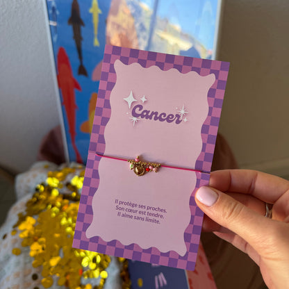 Bracelet Cancer rose à breloque cœur dorée, présenté sur sa carte illustrée