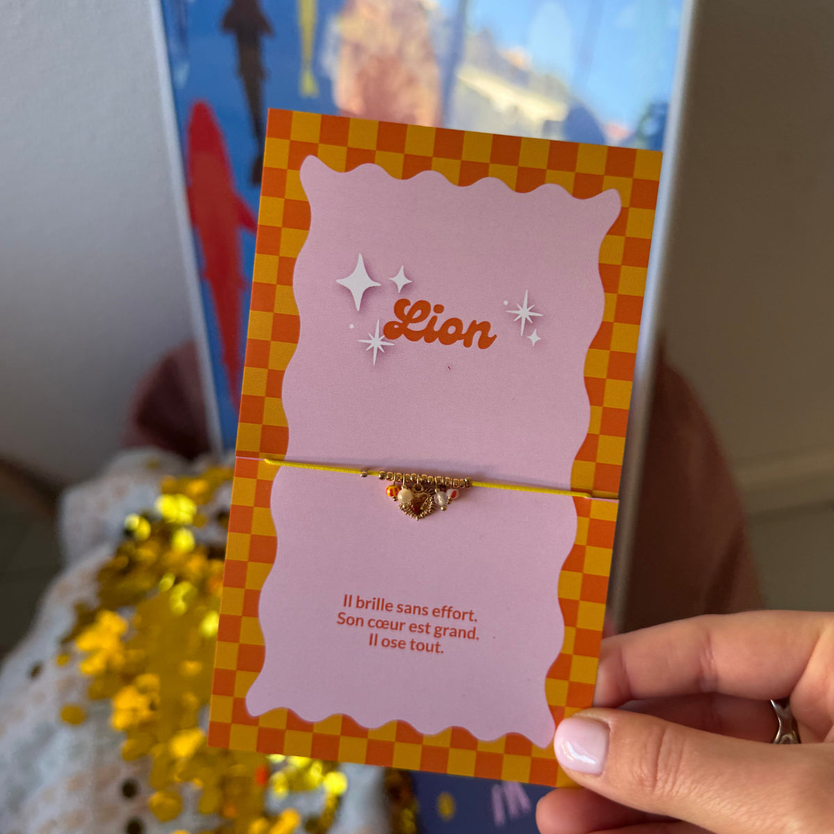 Bracelet Lion doré à breloques, présenté sur une carte rose à carreaux orange