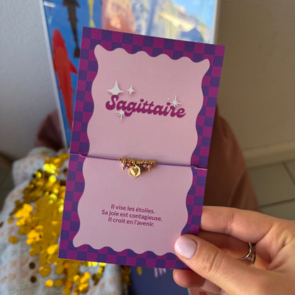 Bracelet Sagittaire doré à breloque cœur, présenté sur une carte à damier violet