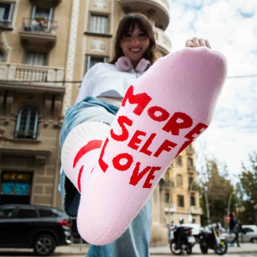 Gros plan sur une chaussette rose pâle « More Self Love » aux lettres rouges