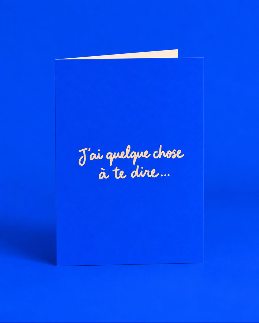 Carte bleue ouverte avec l’inscription manuscrite « J’ai quelque chose à te dire
